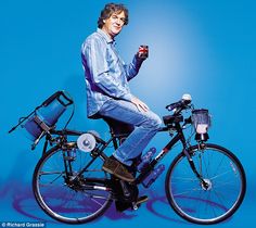 a man sitting on top of a bike holding an object in one hand and smiling at the camera