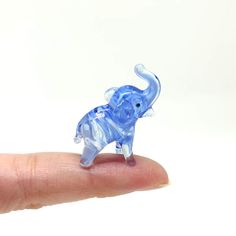 a small blue elephant figurine sitting on top of a persons finger in front of a white background