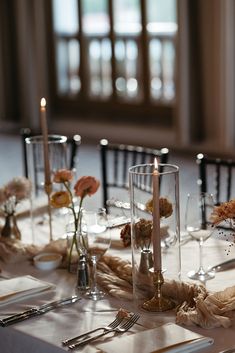 the table is set with silverware, candles and flowers in glass vases on it