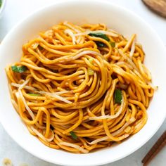 a white bowl filled with noodles and vegetables on top of a table next to chopsticks