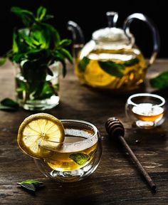 two glasses filled with tea and lemon on top of a wooden table