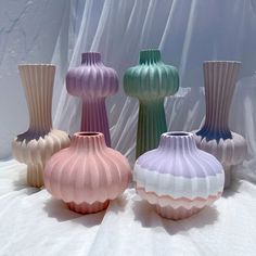 four different colored vases sitting on top of a white cloth covered table next to each other