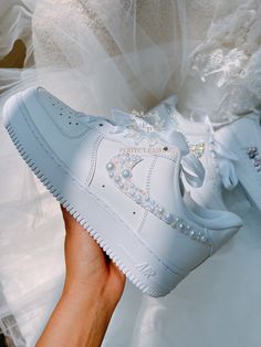 a person holding up a white sneaker with pearls on the side and bows at the top