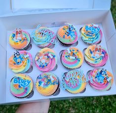 a box filled with lots of cupcakes covered in rainbow frosted icing