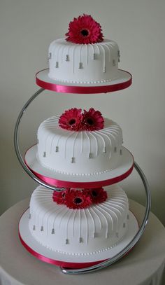 three tiered wedding cake with pink flowers on each layer and red ribbon at the bottom