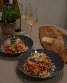 two plates of spaghetti with parmesan cheese and wine on the table next to them