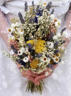 a woman holding a bouquet of wild flowers in her hands with white lace on the sleeves