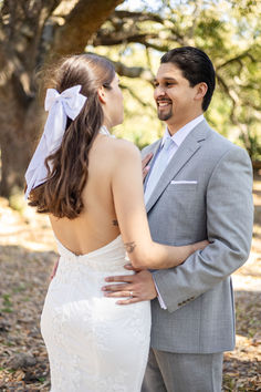 a bride and groom standing together in the woods looking at each other with smiles on their faces