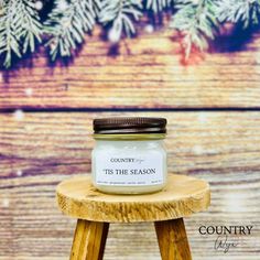 a candle sitting on top of a wooden stool in front of a pine tree with the words country tis the season