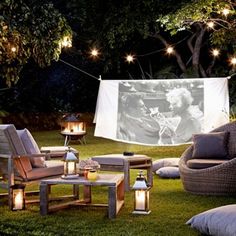 an outdoor movie is set up in the grass with chairs and tables around it, surrounded by string lights