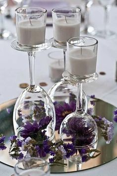 there are four wine glasses on the table with candles in them and some purple flowers