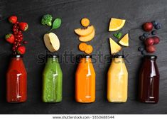 six different types of juice in bottles lined up on a black surface with various fruits and vegetables