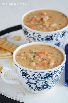 two cups of soup on a plate with crackers and a blue napkin next to it