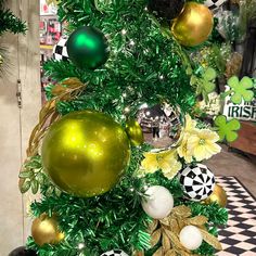 a green and gold christmas tree with ornaments on it's top, surrounded by black and white checkered flooring