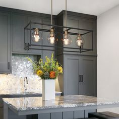 a kitchen with gray cabinets, marble counter tops and pendant lights over the island area