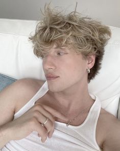 a young man laying on top of a white couch next to a blue pillow and wearing a necklace