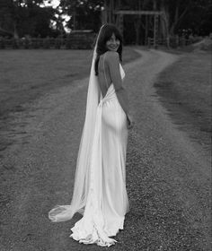 a woman in a wedding dress standing on a dirt road with her back to the camera