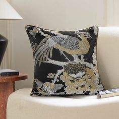 a black and gold pillow sitting on top of a white chair next to a lamp