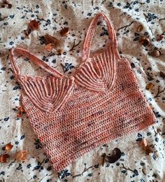 an orange knitted bralet laying on top of a white bed covered in leaves