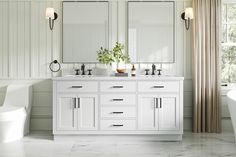 a white bathroom with two sinks, mirrors and a bathtub in it's center