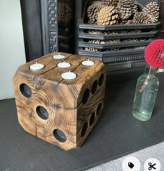 a wooden block sitting next to a vase filled with pine cones and votives