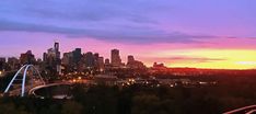 the sun is setting over a city with tall buildings in the foreground and a roller coaster on the other side