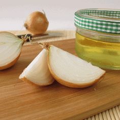 an onion and garlic on a cutting board next to a jar of olive oil with a knife