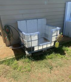 an empty trailer sitting in the grass next to a house with a hose attached to it