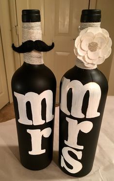 two black bottles with white letters and a flower on the top, one has a moustache