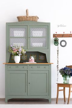 a green hutch with flowers and vases on it in front of a white wall