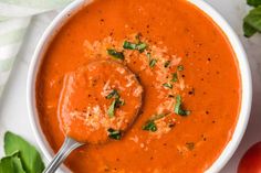 a white bowl filled with tomato soup and garnished with parmesan cheese