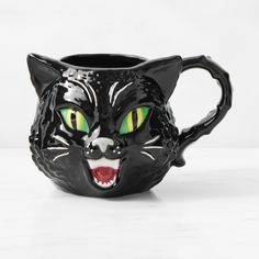 a black cat mug with green eyes and fangs on it's face is shown