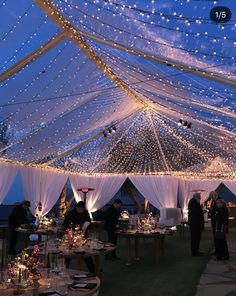 the inside of a tent with tables and chairs covered in white draping at night