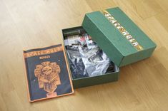 an open green box on top of a wooden floor next to a book and some papers