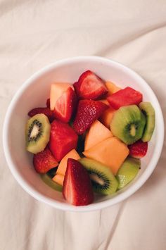 a white bowl filled with cut up fruit on top of a tablecloth covered bed