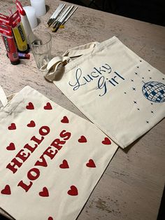 two totes bags sitting on top of a wooden table next to bottles and utensils