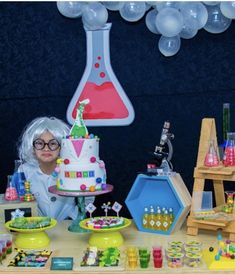 a woman sitting in front of a table with a cake on it and some balloons