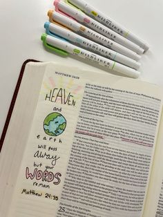 an open bible with markers and pens on it next to some other writing materials that include crayons