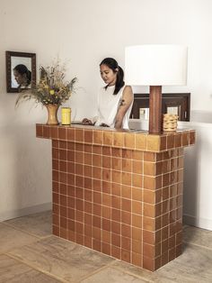 a woman standing behind a counter with a vase on top of it next to a mirror