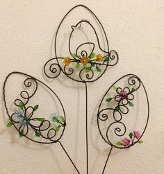 three metal flowers with leaves and vines in the shape of hearts on a white wall