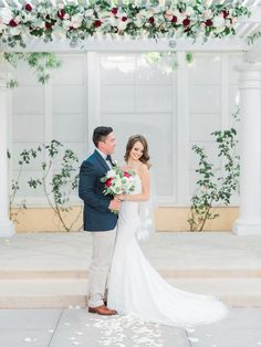 a bride and groom standing under an arch with flowers