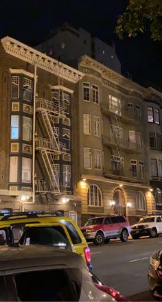 cars are parked on the street in front of an apartment building with fire escape stairs