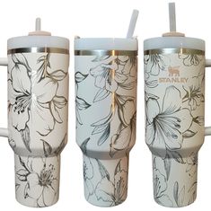 three travel mugs with floral designs on the sides, one has a straw in it