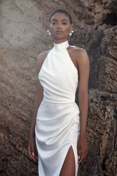 a woman in a white dress standing next to a rock