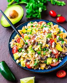 a bowl filled with pasta salad next to sliced avocado