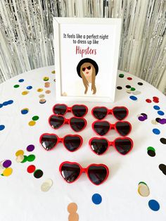 red heart shaped sunglasses sitting on top of a table next to a card and confetti