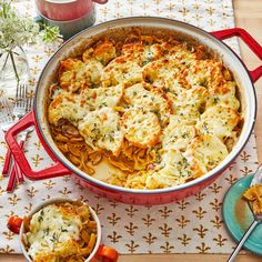 a casserole dish with cheese and vegetables in it on a table next to two plates