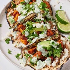 three tacos on a white plate with limes and cilantro wedges