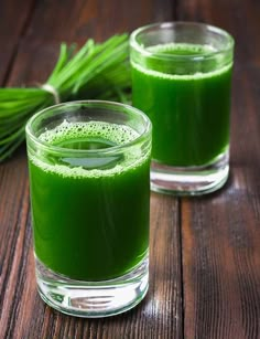 two glasses filled with green liquid on top of a wooden table