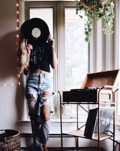 a woman standing in front of a window with a record on her head and ripped jeans